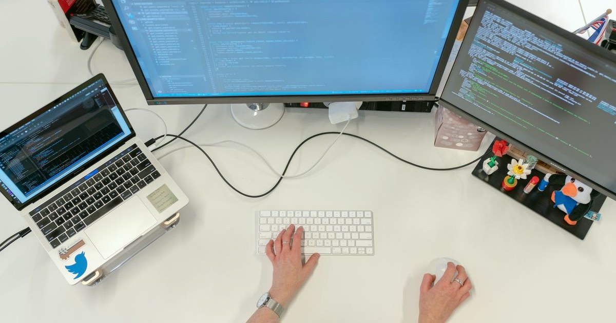 Software developer writing code on dual monitors and a laptop, representing the choice to build your own travel website