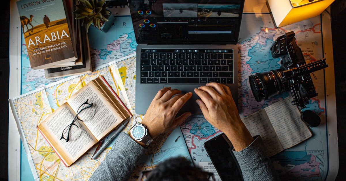 Travel professional planning itineraries at a desk with a laptop, Europe map and research notes, representing B2B sub-agent booking work