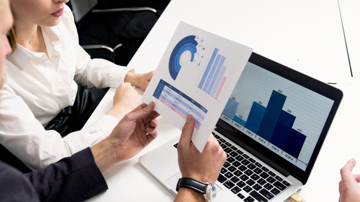 Colleagues reviewing pricing charts and a laptop dashboard, the kind of markup and sales view consolidators use on a B2B travel portal