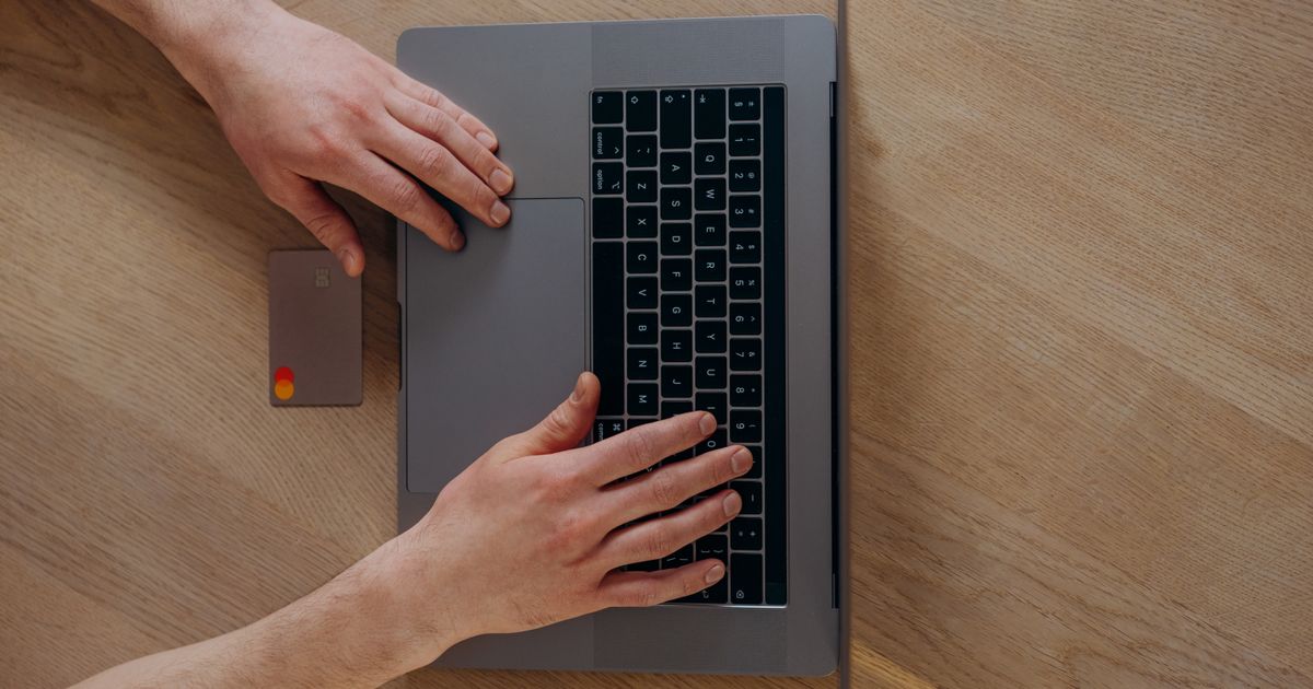 Top-down view of hands typing on a laptop beside a bank card on a wooden desk, representing a customer paying online through a travel agency's payment gateway